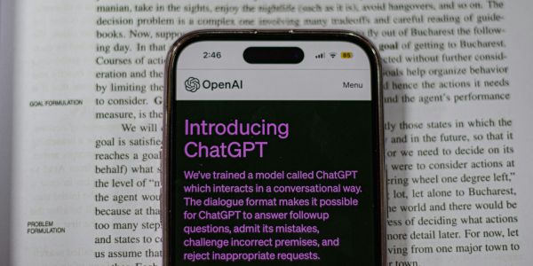 A cell phone set on the page of an open book, ready to use the ChatGPT app for copywriting.